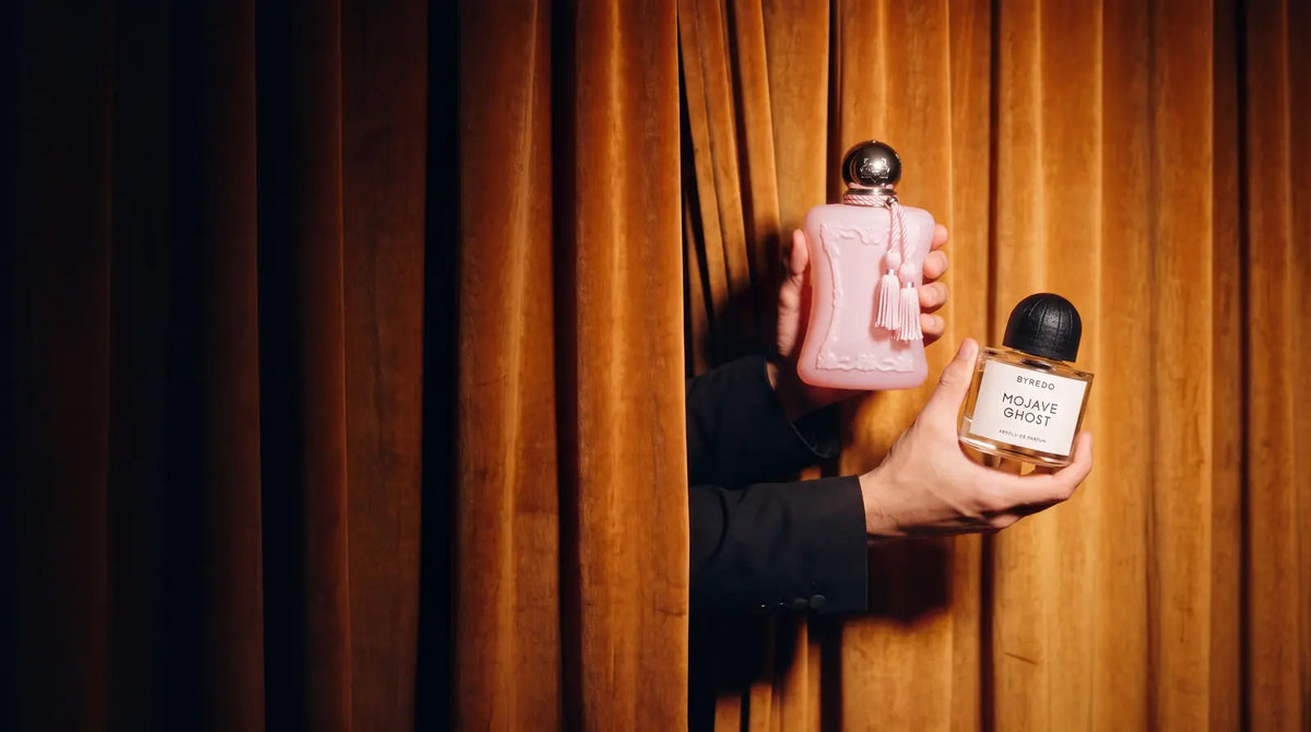 Hands reveal Parfums de Marly Delina and Byredo Mojave Ghost Absolu de Parfum through an amber velvet curtain
